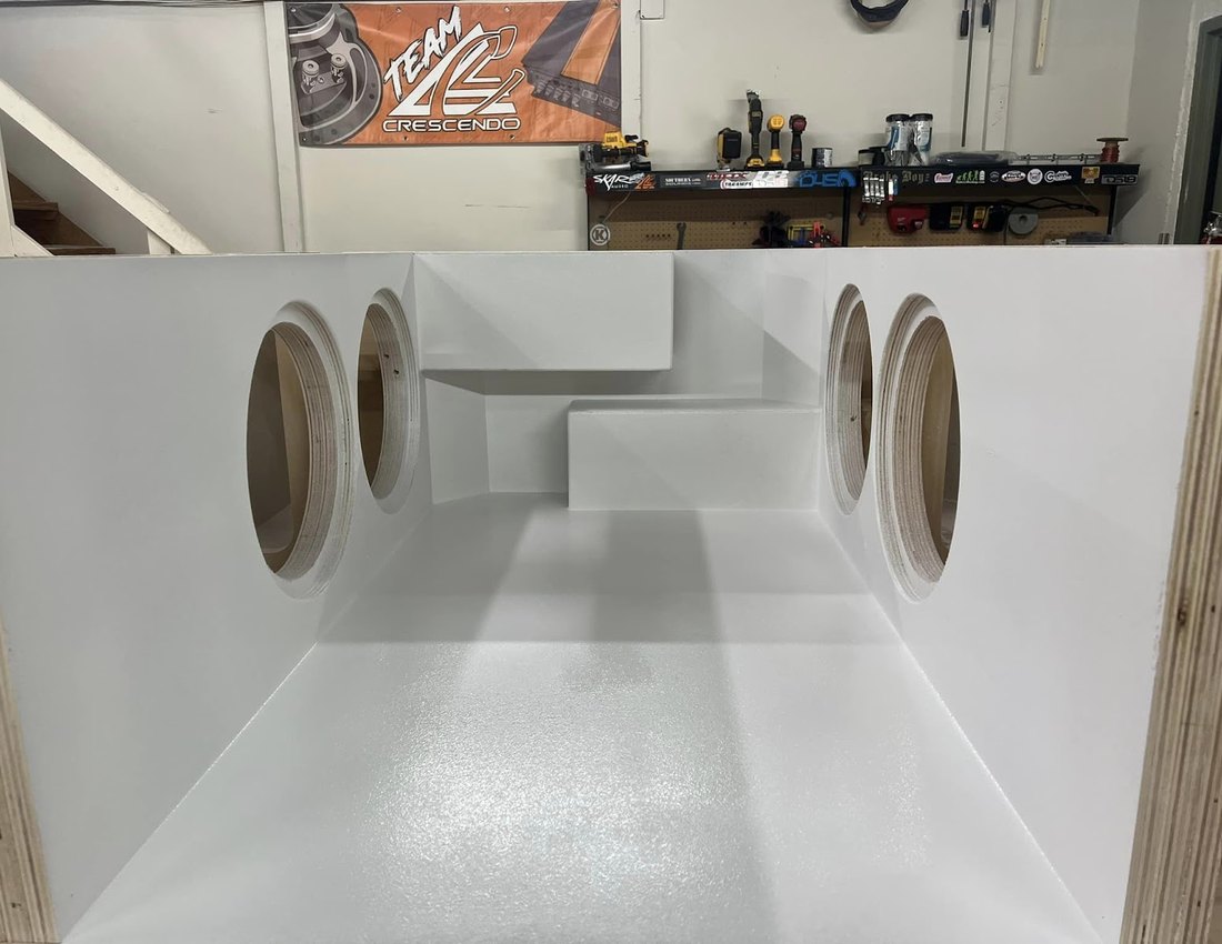 White fiberglass subwoofer enclosure with dual cutouts in progress on the shop bench