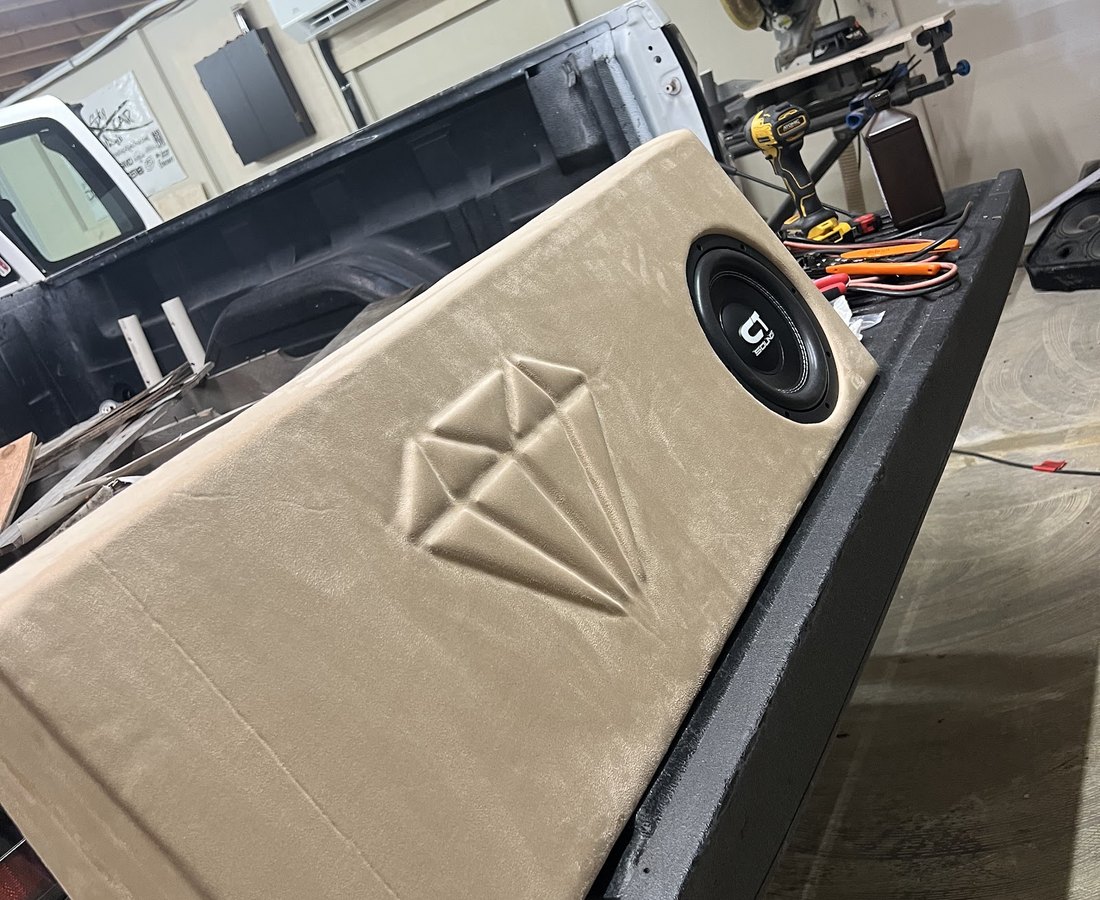 Custom subwoofer enclosure with a diamond-stitched wrap being finished on the shop bench at Voltage Row