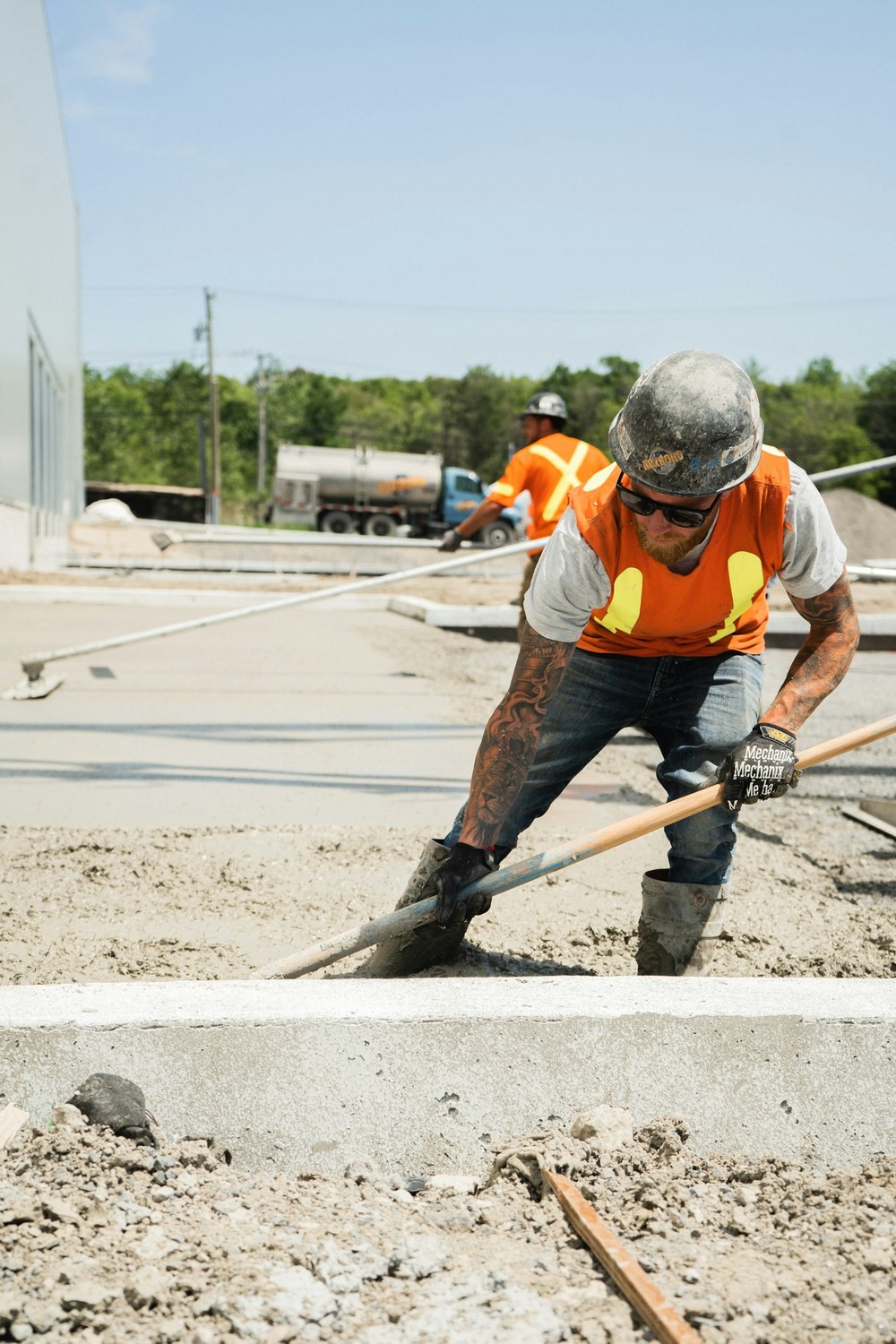 Concrete worker raking and placing fresh concrete against a formed curb edge