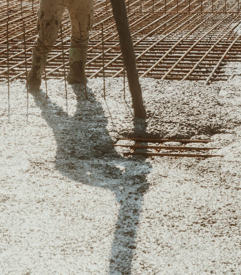 Worker screeding wet concrete across a reinforcing mesh on a new slab pour