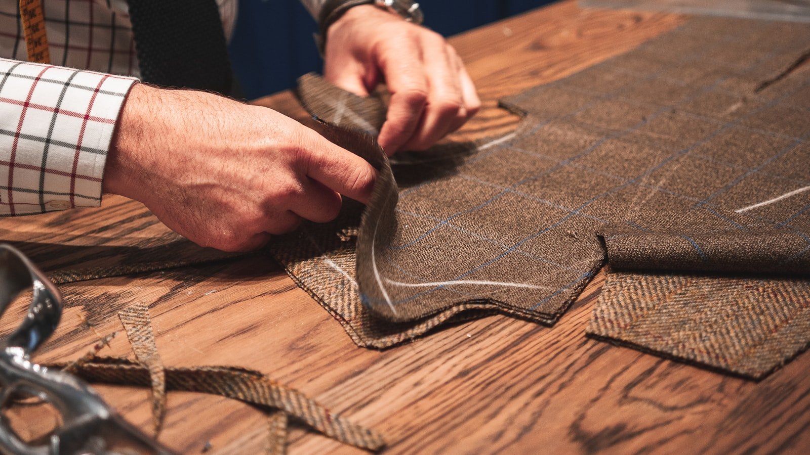 Tailor's hands working a length of tweed fabric at the cutting table