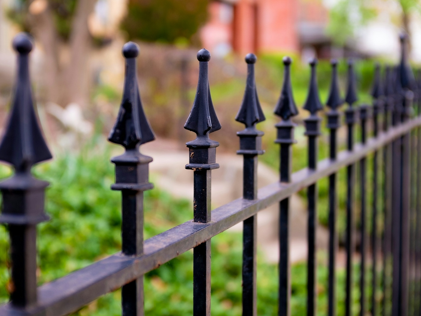 A black ornamental metal fence with spear-tipped finials running along a green garden bed