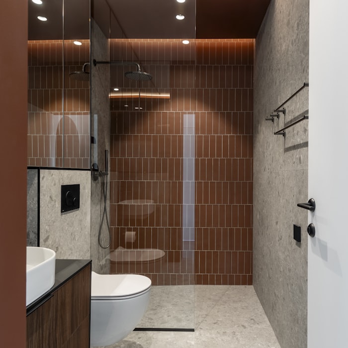 Speckled stone tile floor set in a modern bathroom with a brown tiled shower