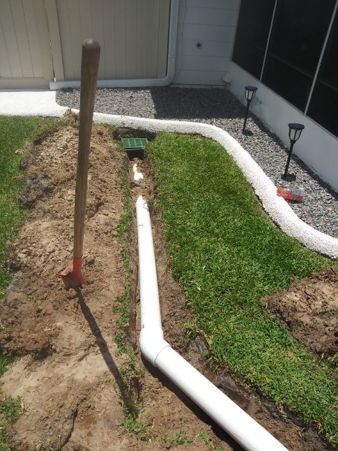 A neat trench with new white irrigation pipe laid in beside the lawn edging