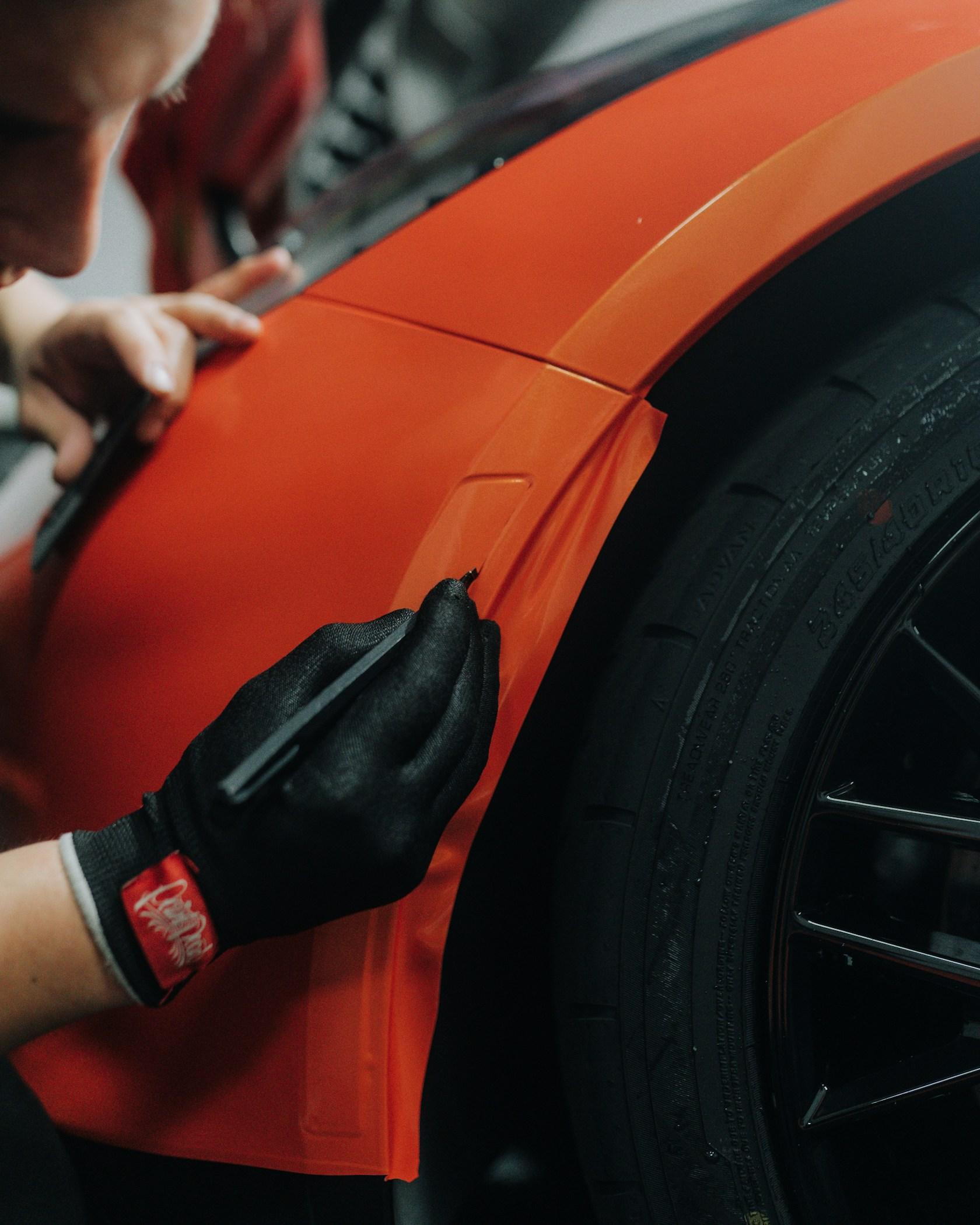 Installer squeegeeing bright orange vinyl graphics onto a vehicle body panel