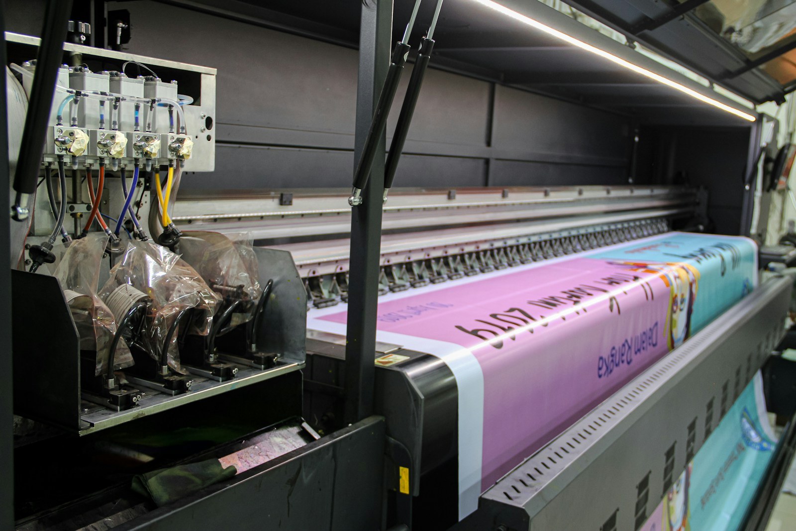 Wide-format printer running a full-colour vinyl banner through the shop