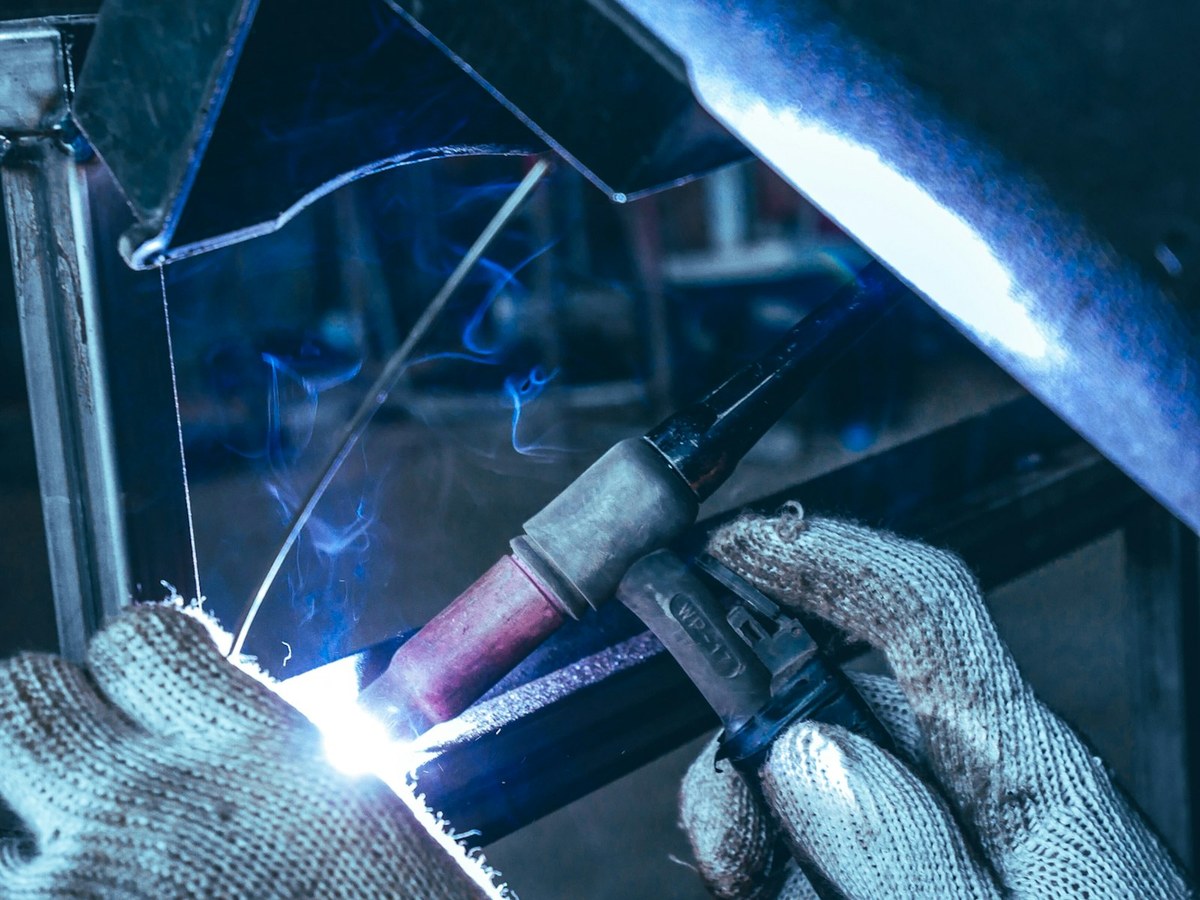 Detail of a gloved welder running a bright MIG weld along a metal joint, blue smoke rising