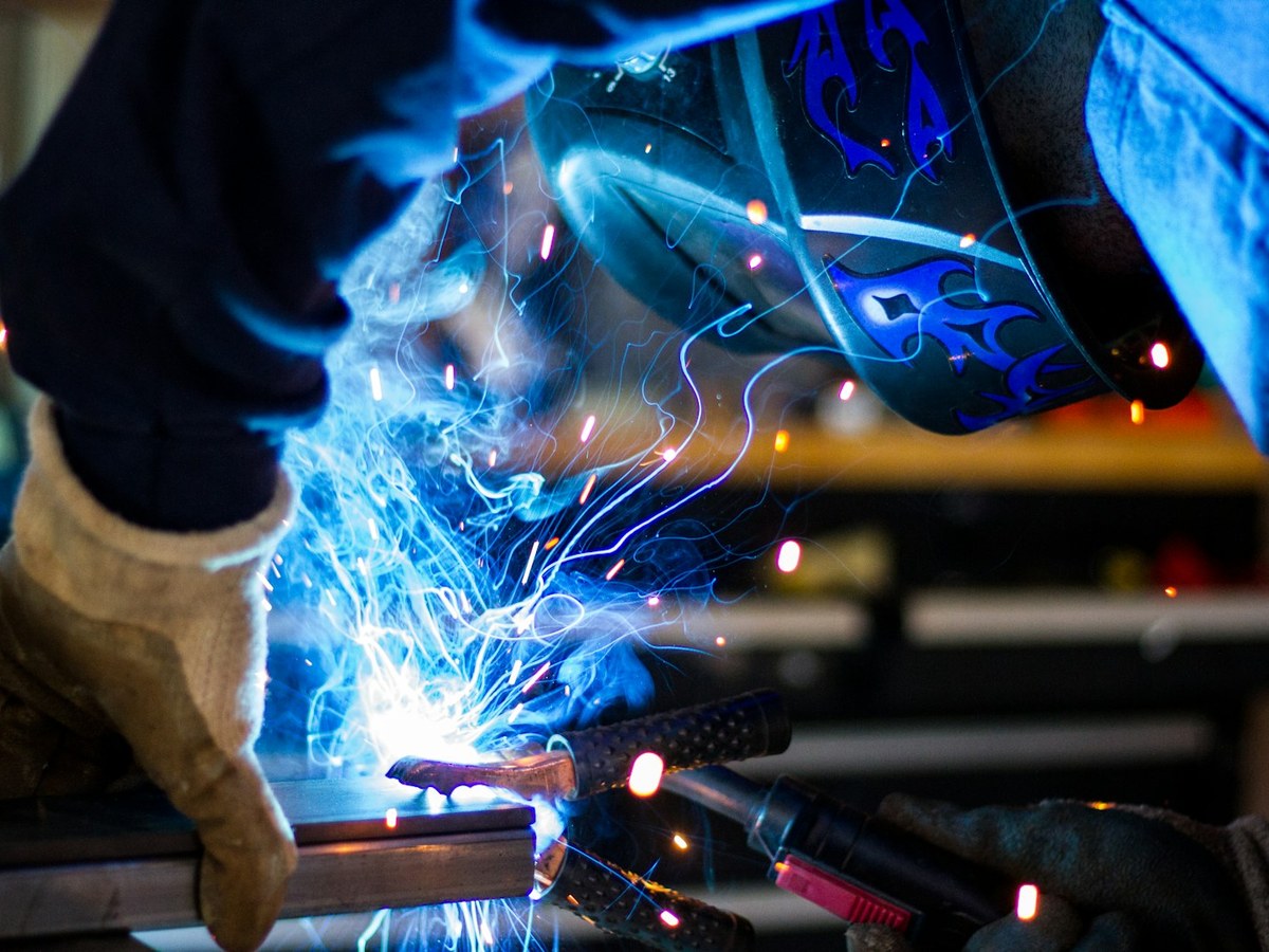 Close-up of a welder in a helmet joining steel with a bright burst of sparks in a fabrication shop